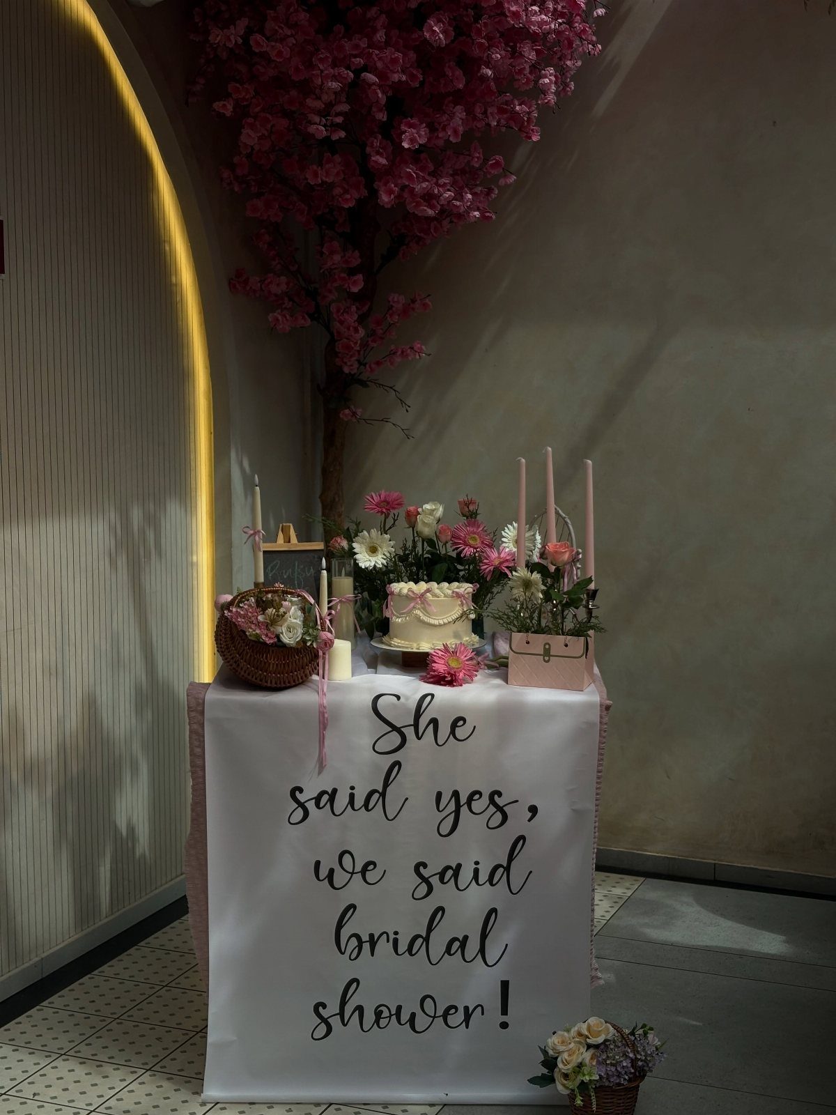Dessert table with a white cake and pink flowers for a bridal shower.