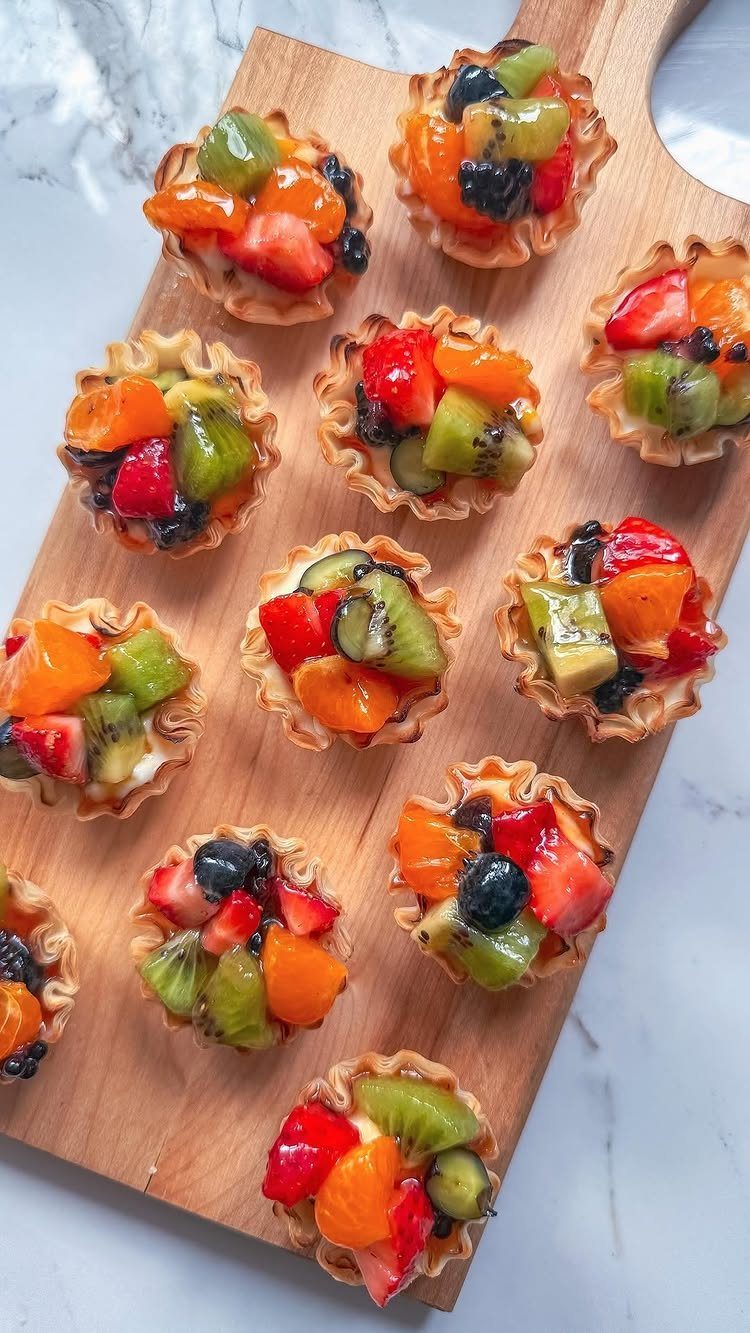 Mini fruit tarts with fresh berries and kiwi on a wooden board