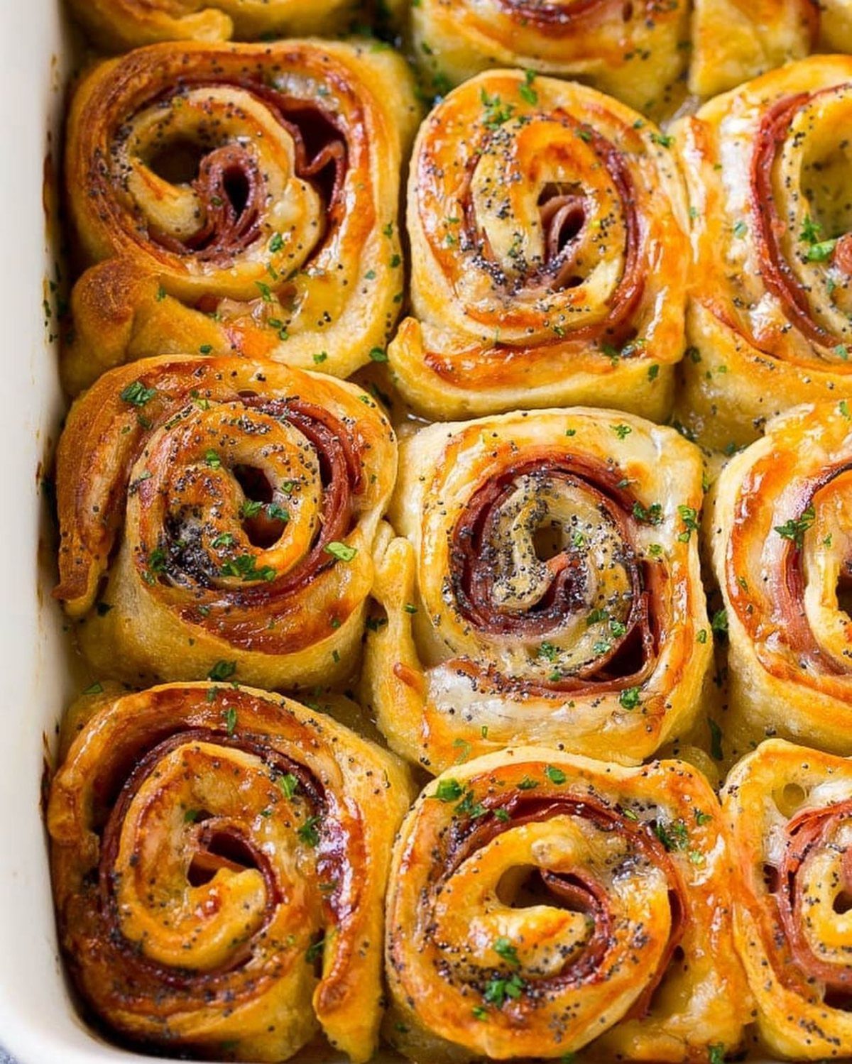 Ham and cheese pinwheels baked in a dish and garnished with fresh parsley.