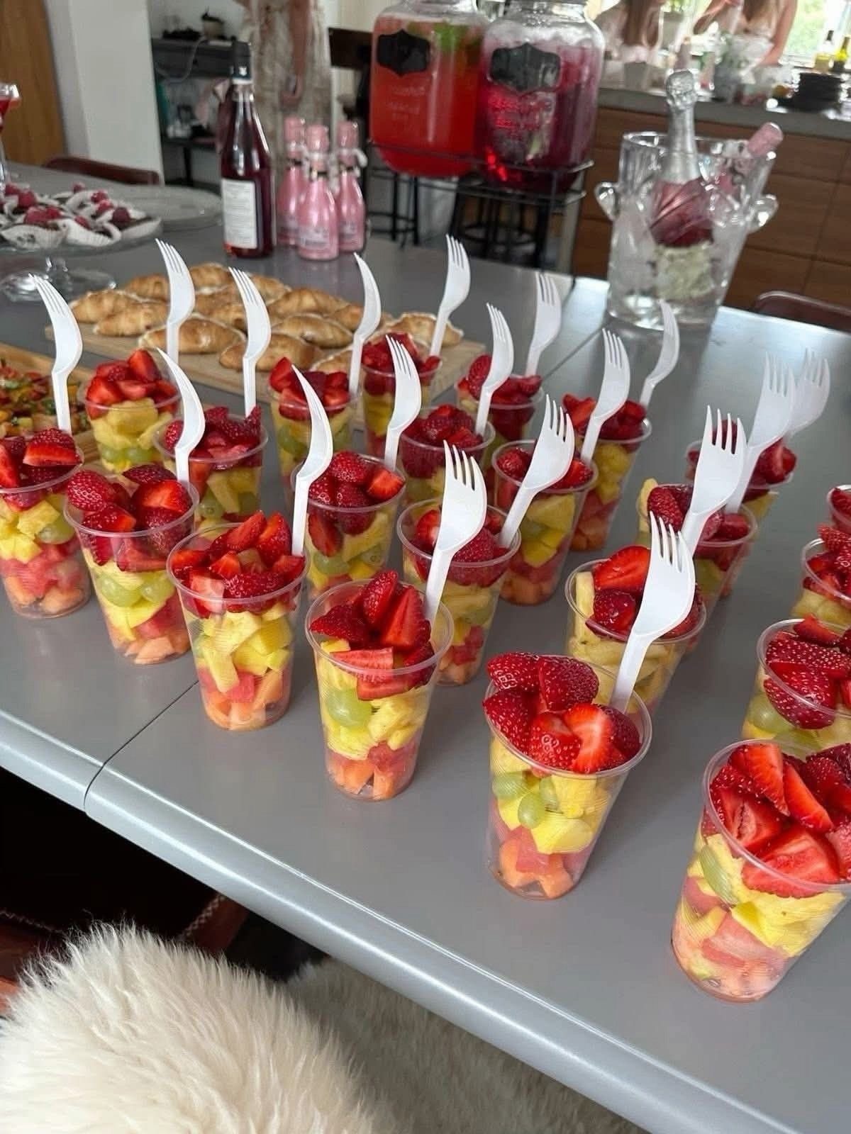 Fruit salad cups with white forks arranged on a grey table for party.