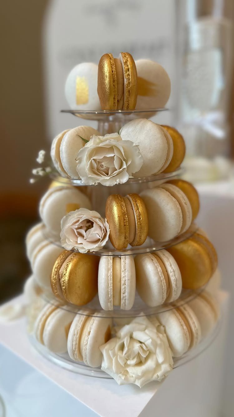 White and gold macarons on a tiered stand decorated with white frosting roses.