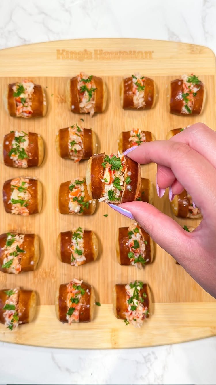 Mini lobster rolls with green herbs on a wooden board being picked up.