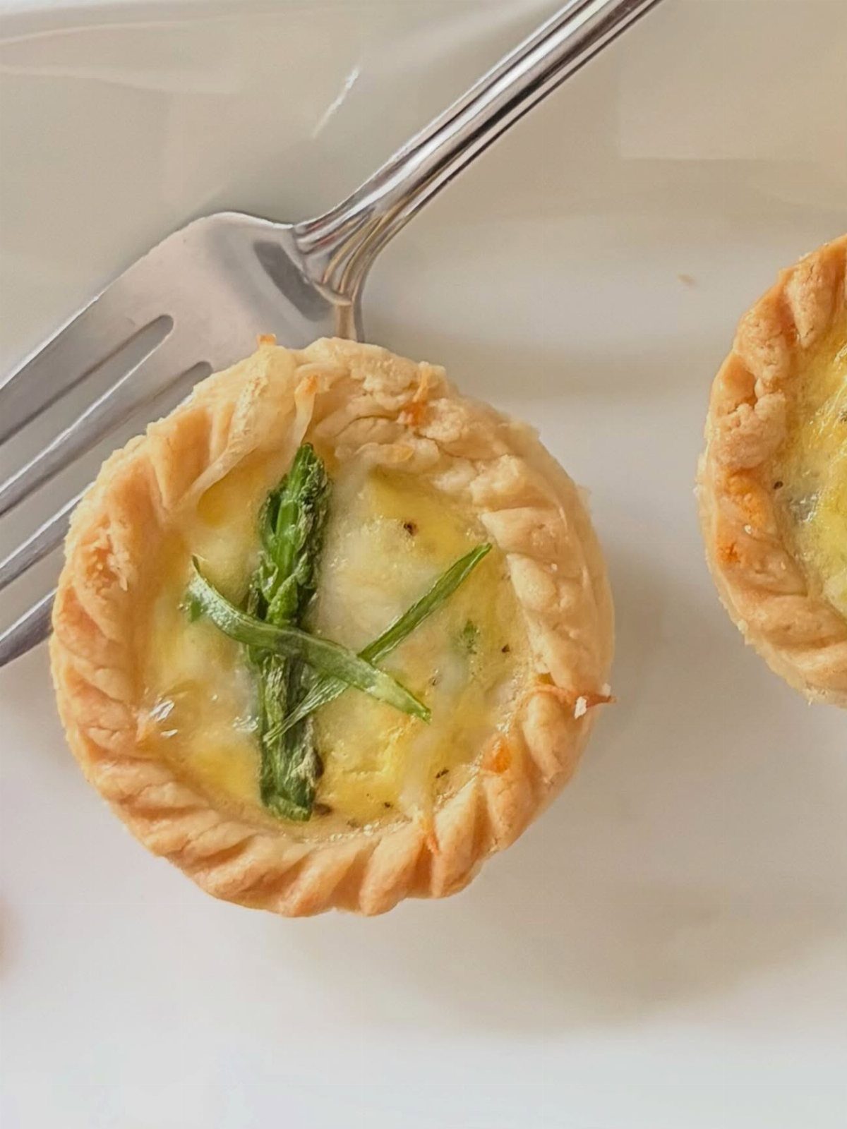 Mini quiches with asparagus spears on a white plate with a silver fork.