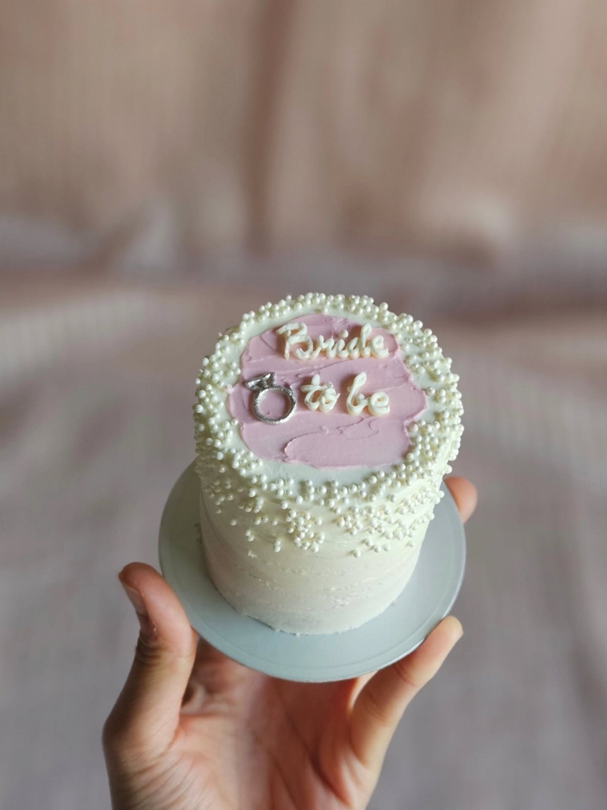 Small white cake with pink frosting and Bride to be text held by hand