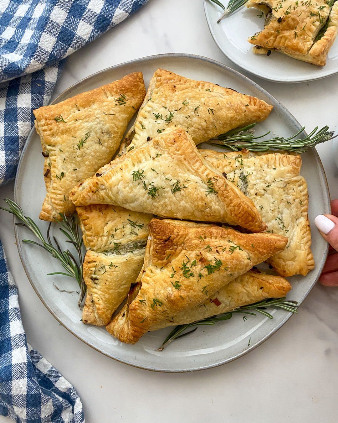 Triangular savory hand pies with herbs on a grey plate with rosemary sprigs.
