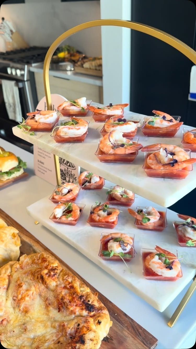 Shrimp cocktail shooters in small clear cups on white marble serving tiers.
