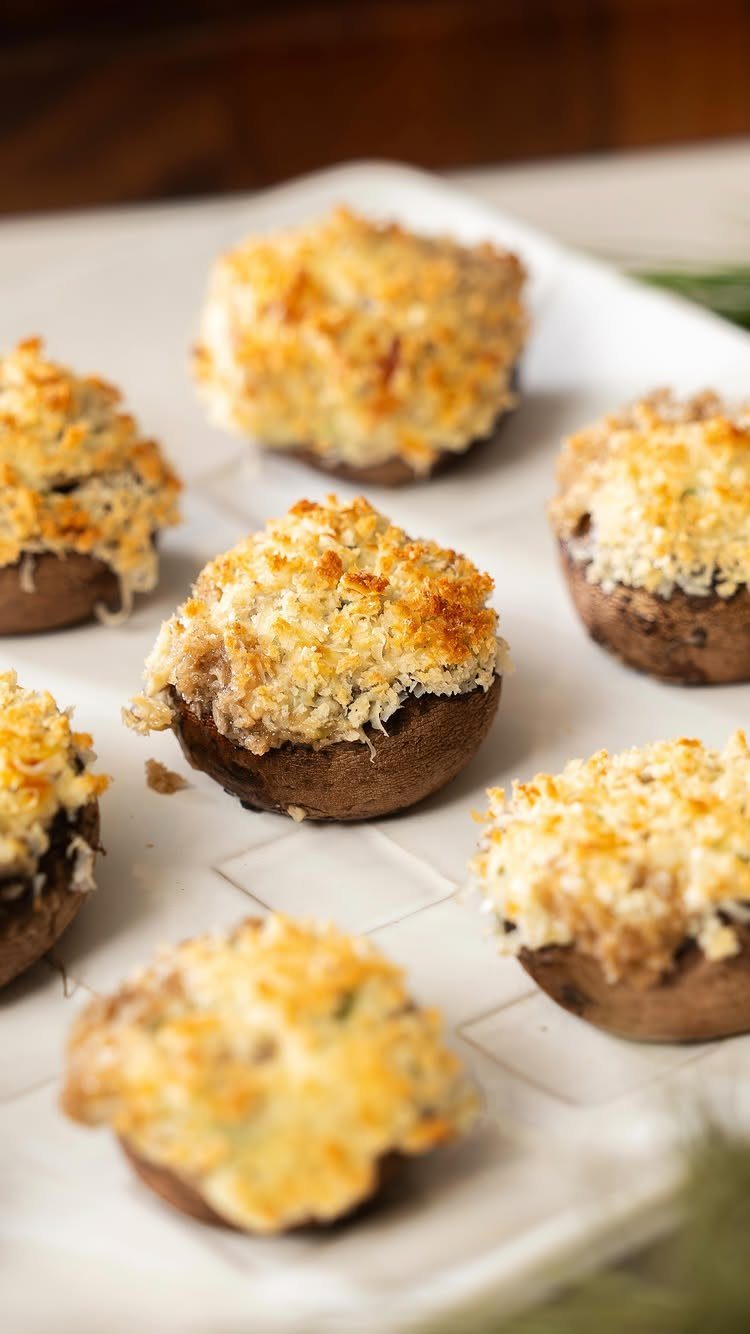 Stuffed mushroom caps with golden toasted cheese topping on a white platter