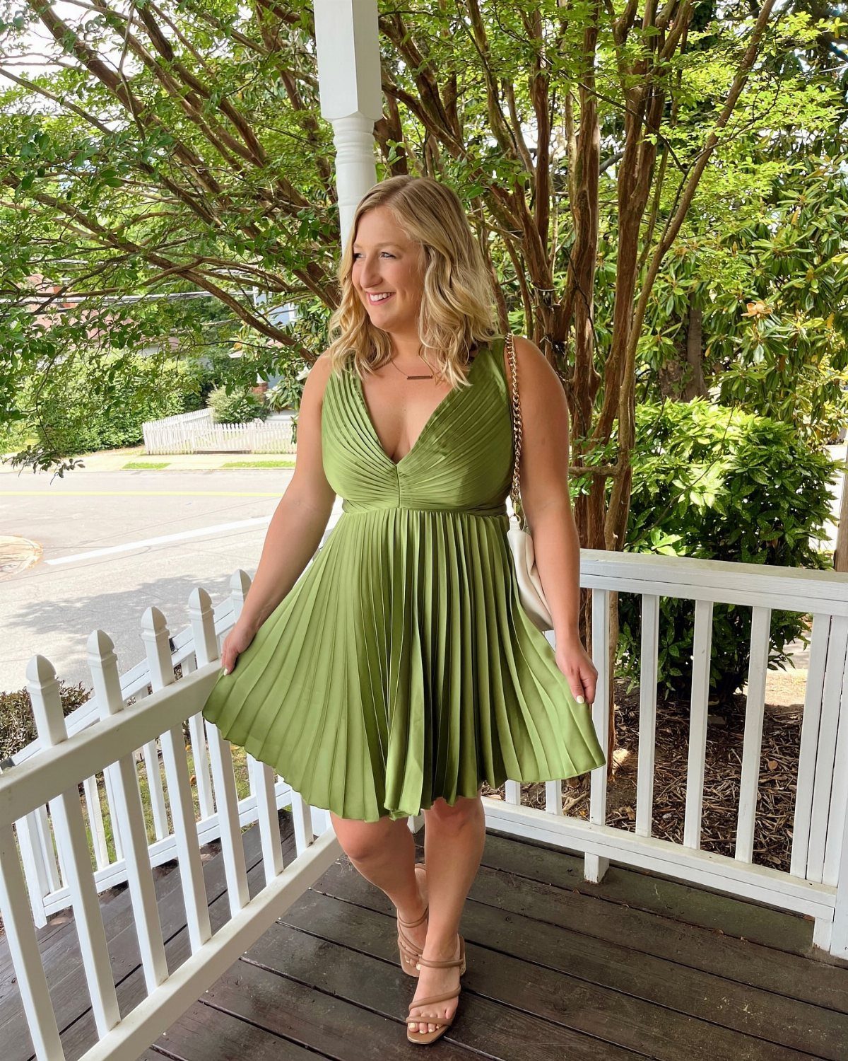 Woman in a pleated olive green mini dress standing on a white porch