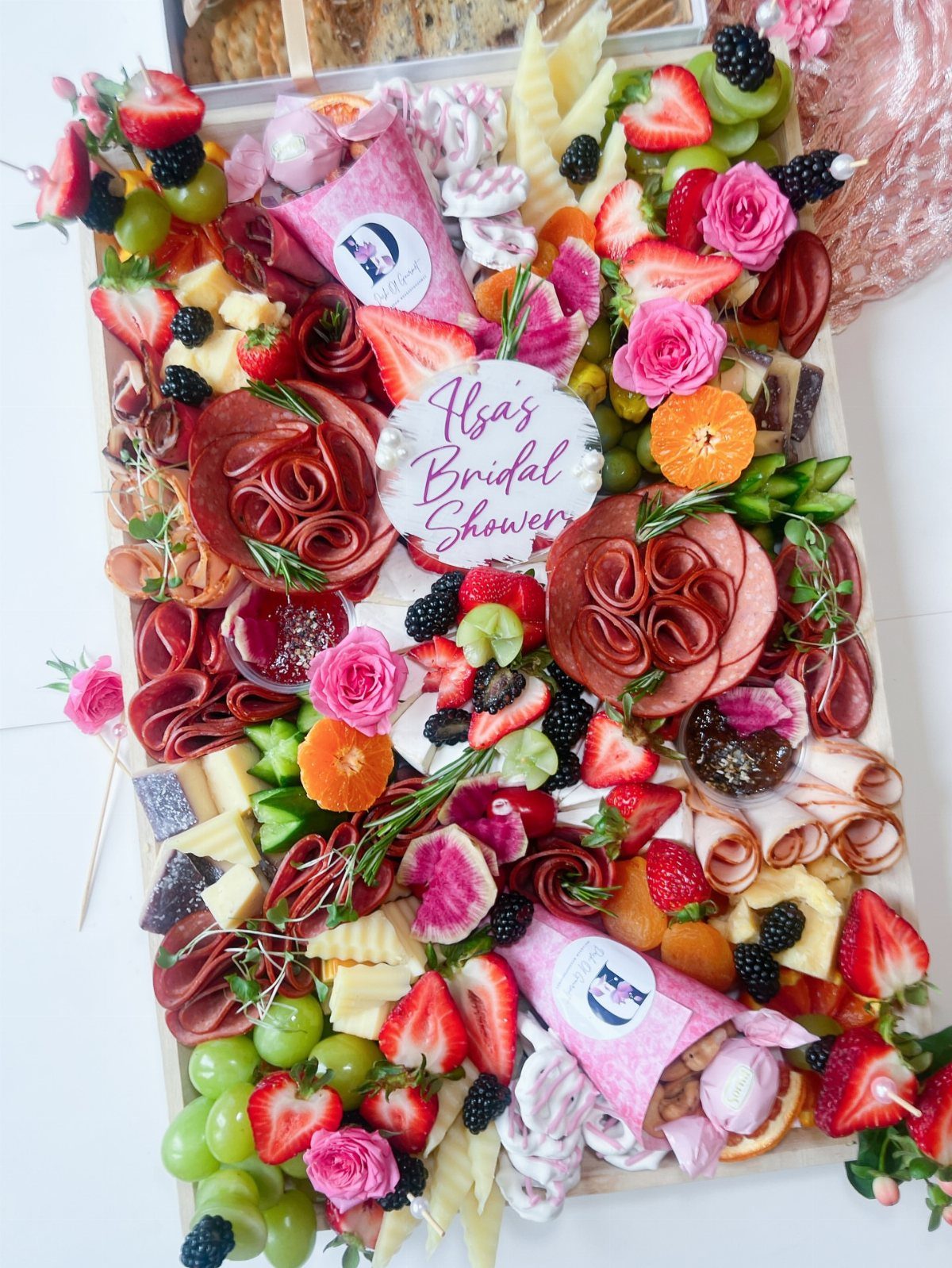 Wooden charcuterie board with meats, cheeses, fruits, and roses for a bridal shower.