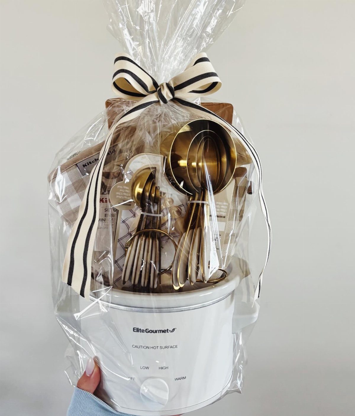 White electric pot gift basket with gold utensils wrapped in clear cellophane.