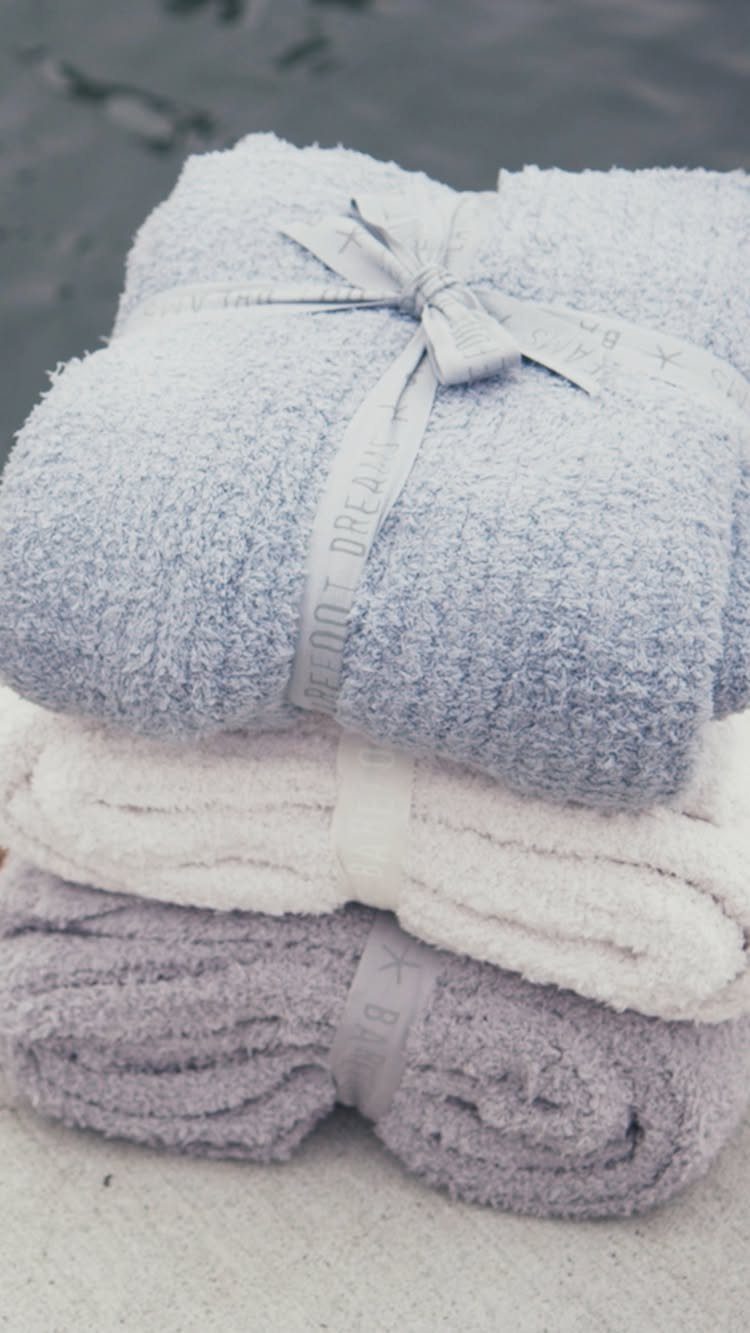 Stacked plush towels in blue, white, and lavender tied with a ribbon bow.