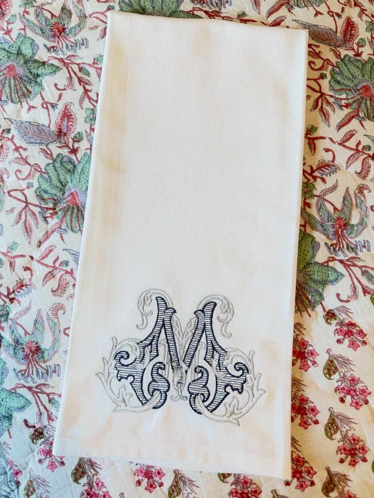 White monogrammed tea towel with an ornate grey letter M on floral fabric