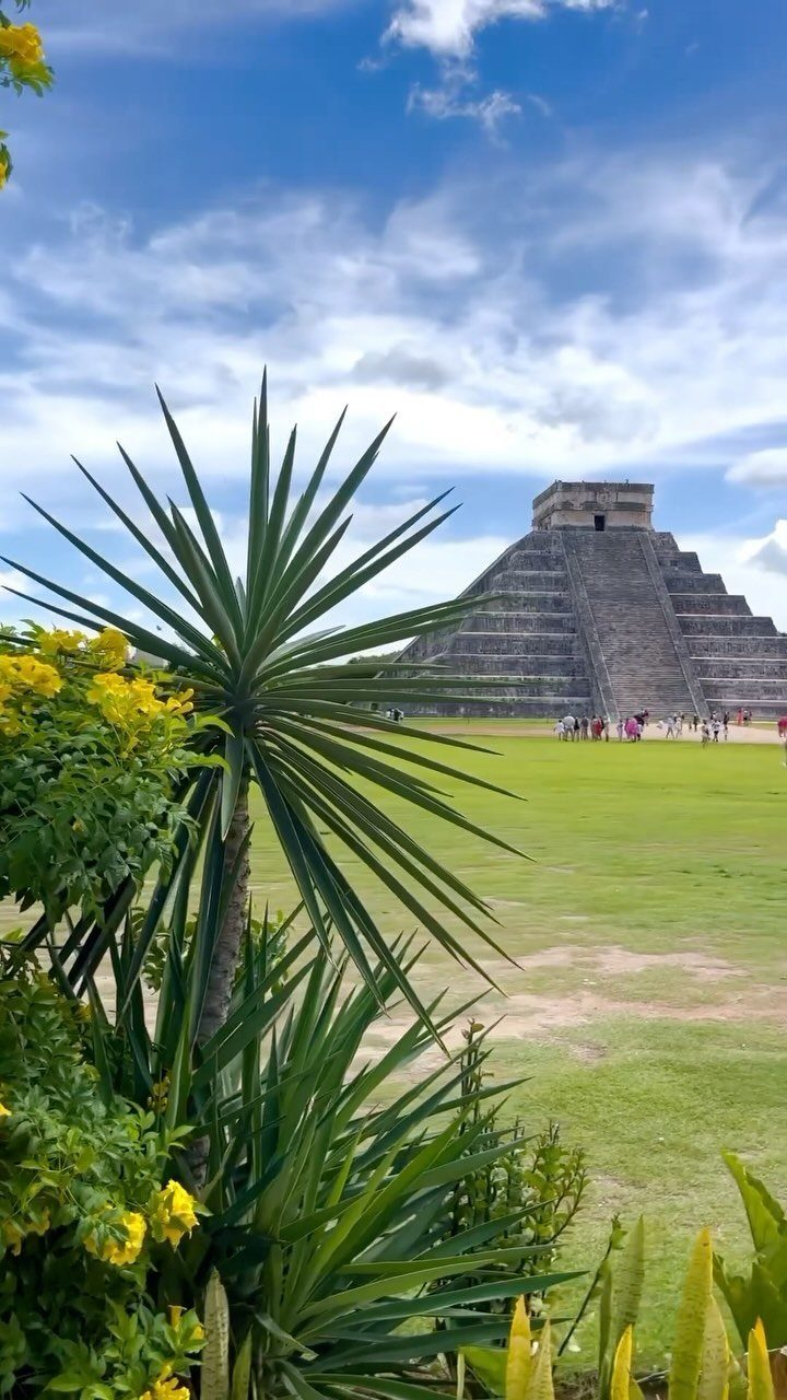 Mayan pyramid at Chichen Itza viewed through green foliage and yellow flowers.