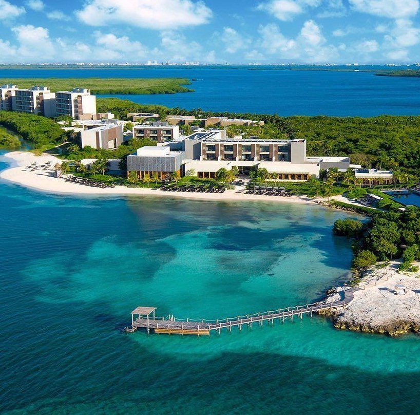 Luxury resort buildings and a wooden pier on a turquoise beach in Cancun.