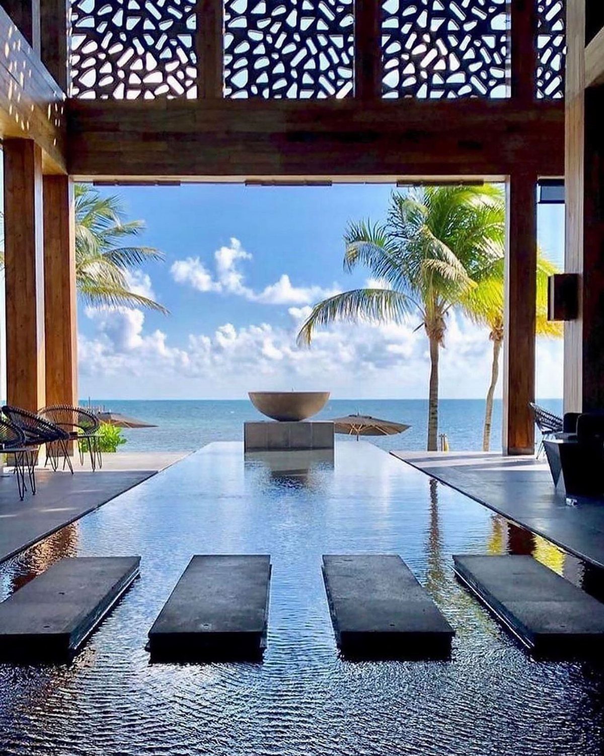 Luxury infinity pool overlooking a tropical beach with palm trees and turquoise ocean.
