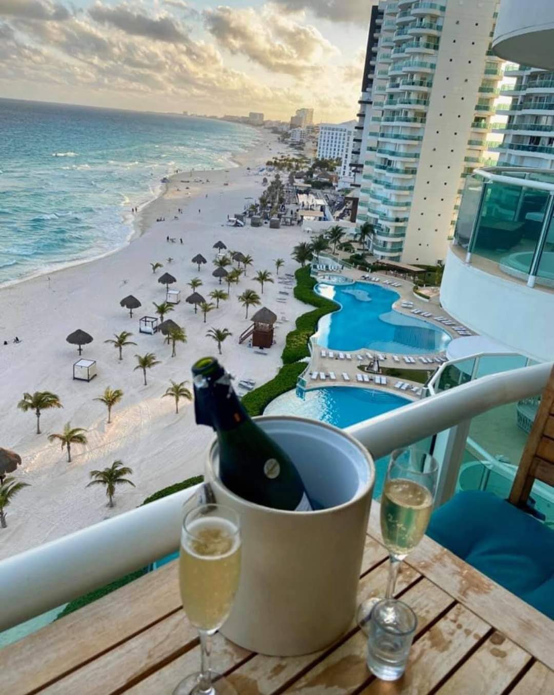 Champagne glasses and bottle on a balcony overlooking a Cancun beach resort.