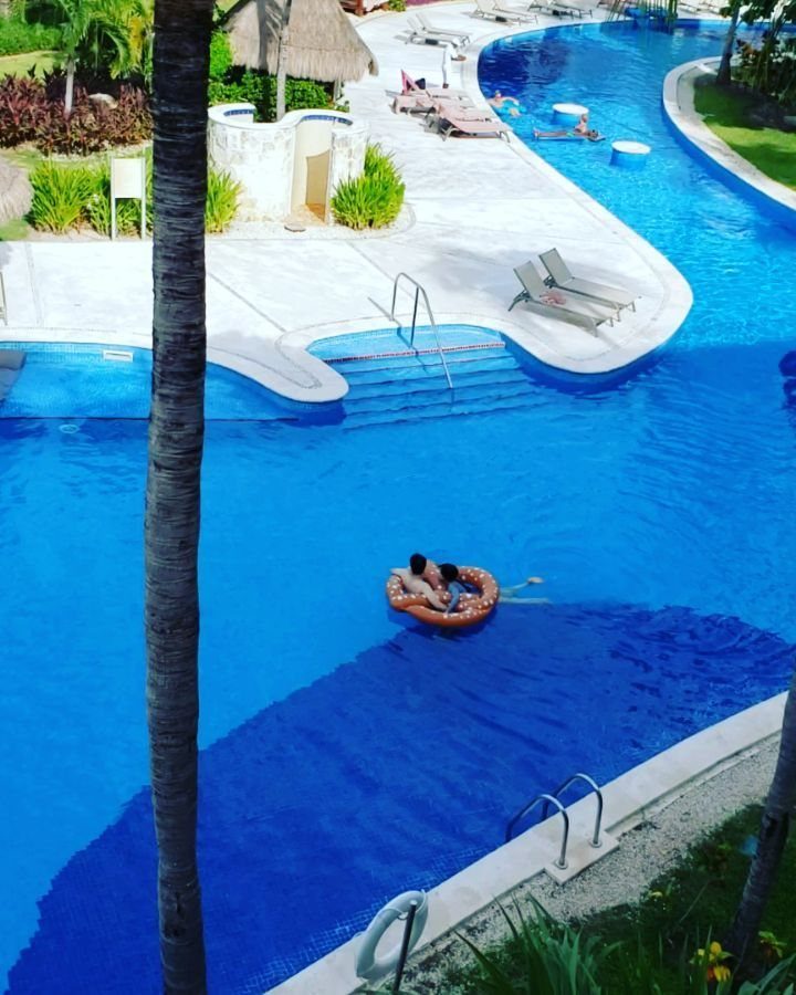 Couple floating in an orange tube in a bright blue resort swimming pool