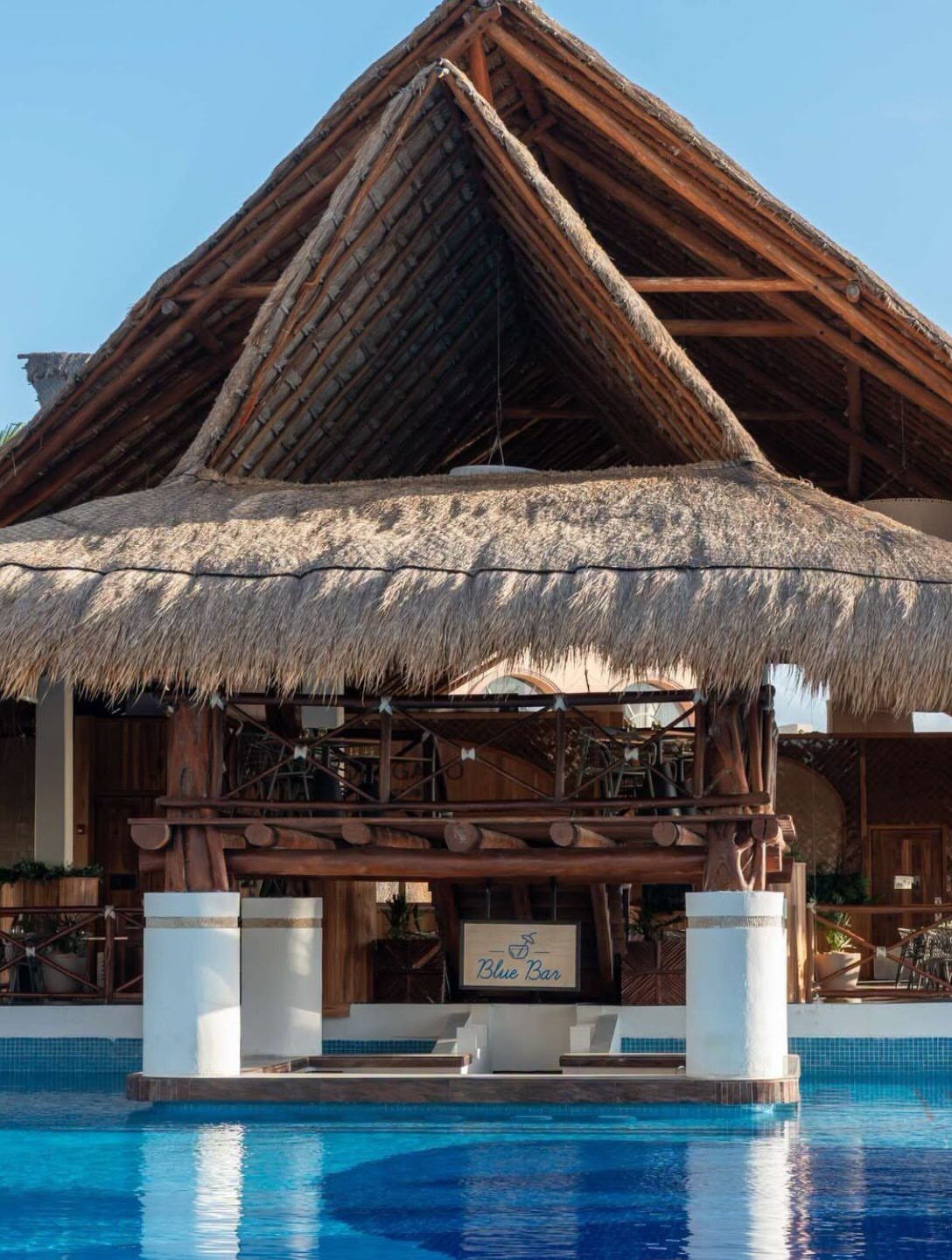 Swim-up bar with a thatched roof and blue pool under a clear sky