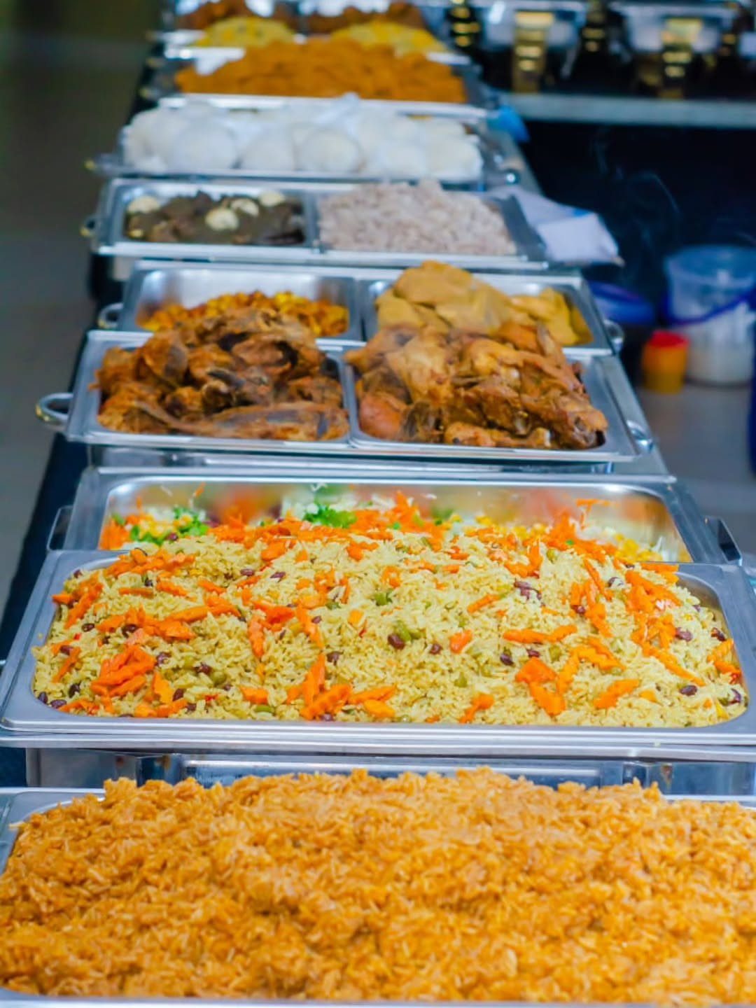 Buffet line of stainless steel trays filled with rice and meat dishes.