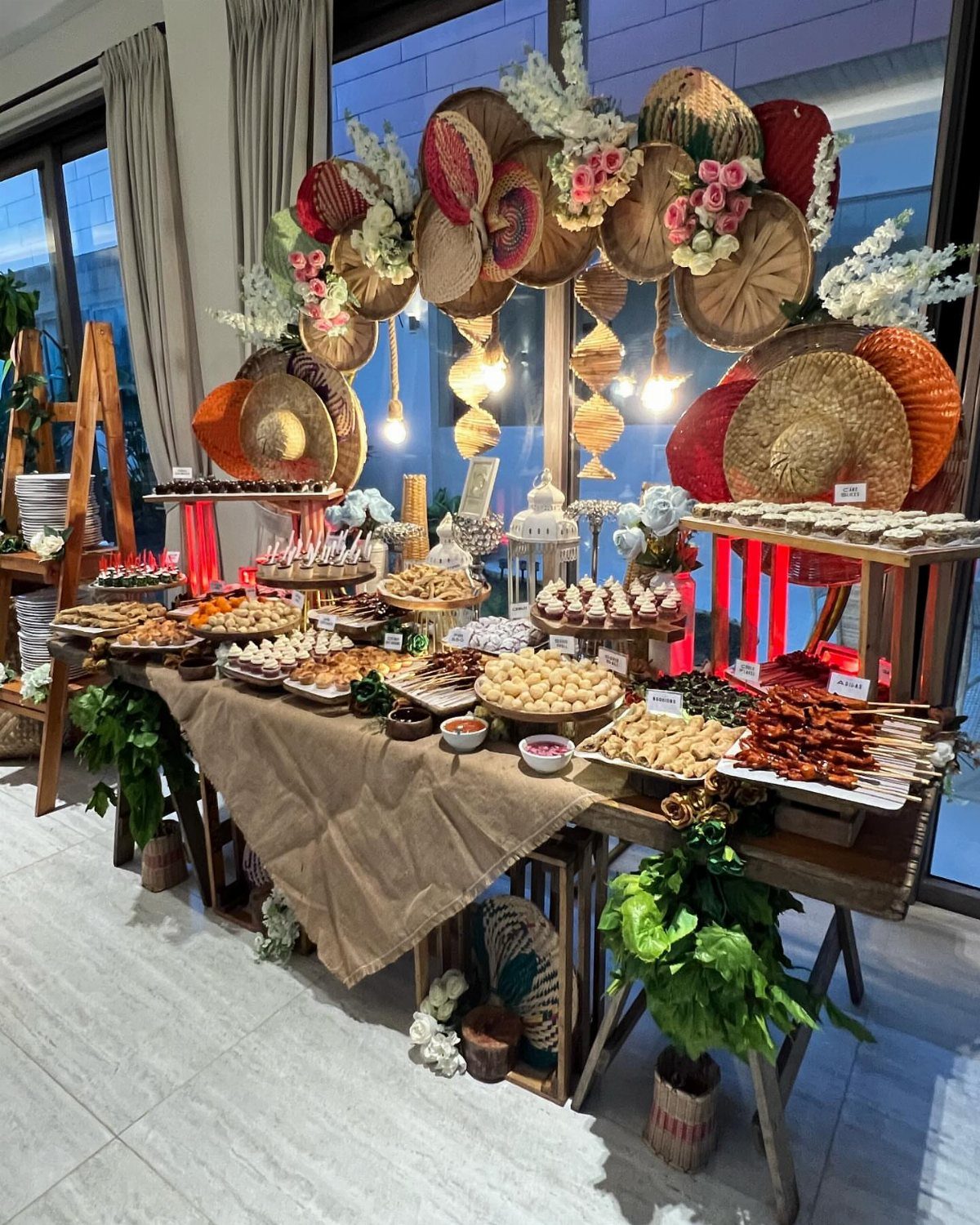 Catering table with appetizers and skewers decorated with traditional woven hats and lanterns