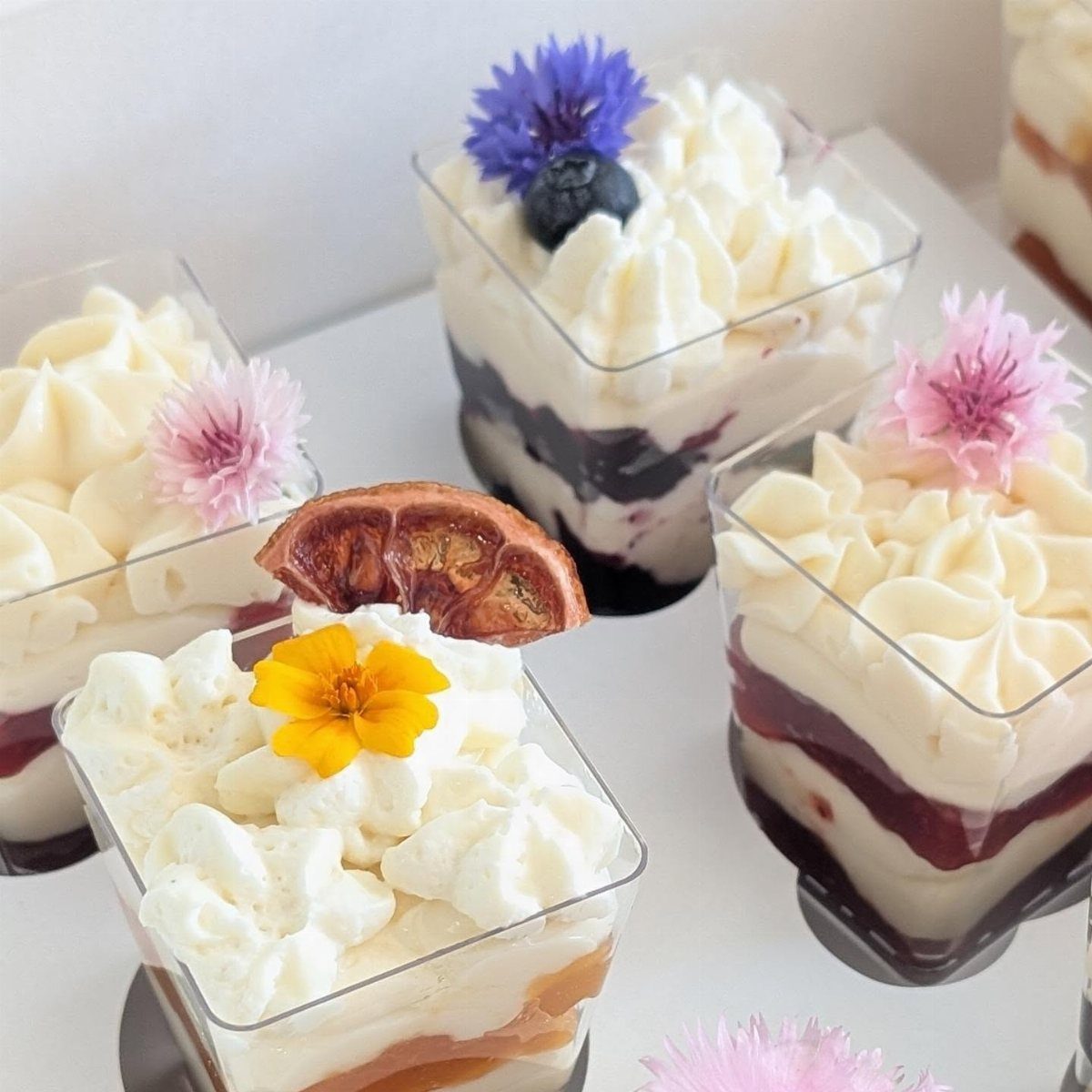 Layered dessert cups topped with whipped cream and colorful edible flowers