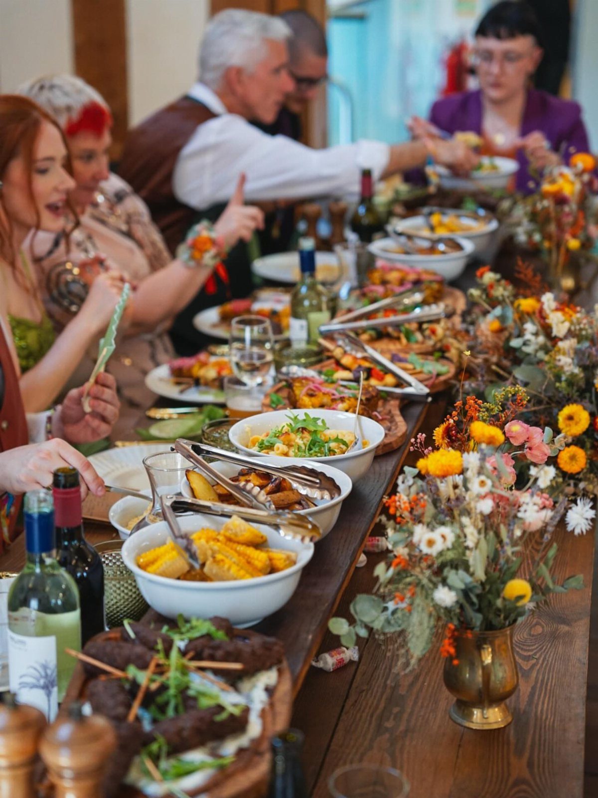 Long wooden table with shared platters of food and guests dining together.