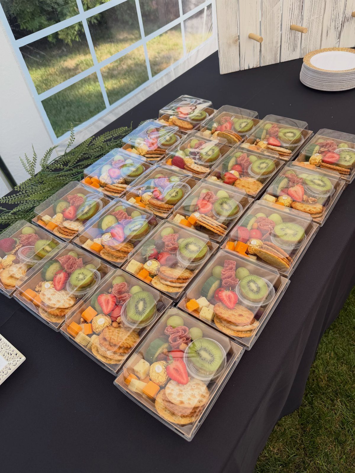 Individual charcuterie boxes with fruit, cheese, and crackers on a black table.