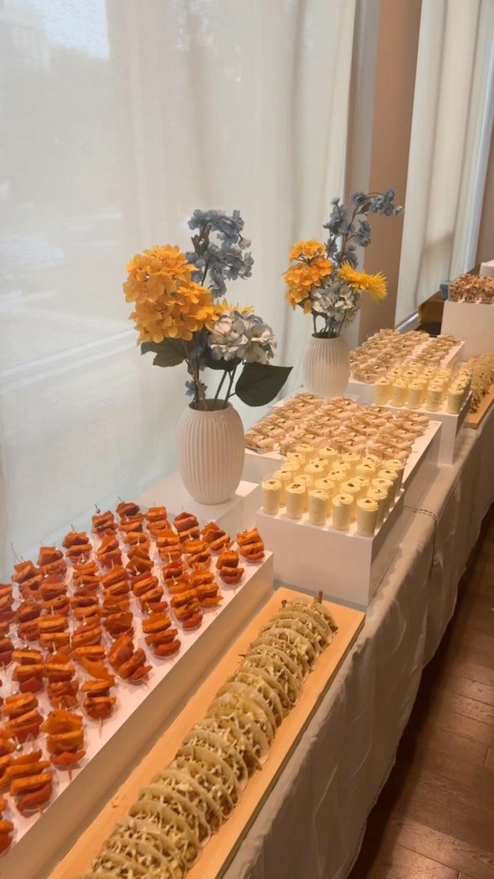 Catering table with assorted miniature appetizers and desserts decorated with yellow and blue flowers