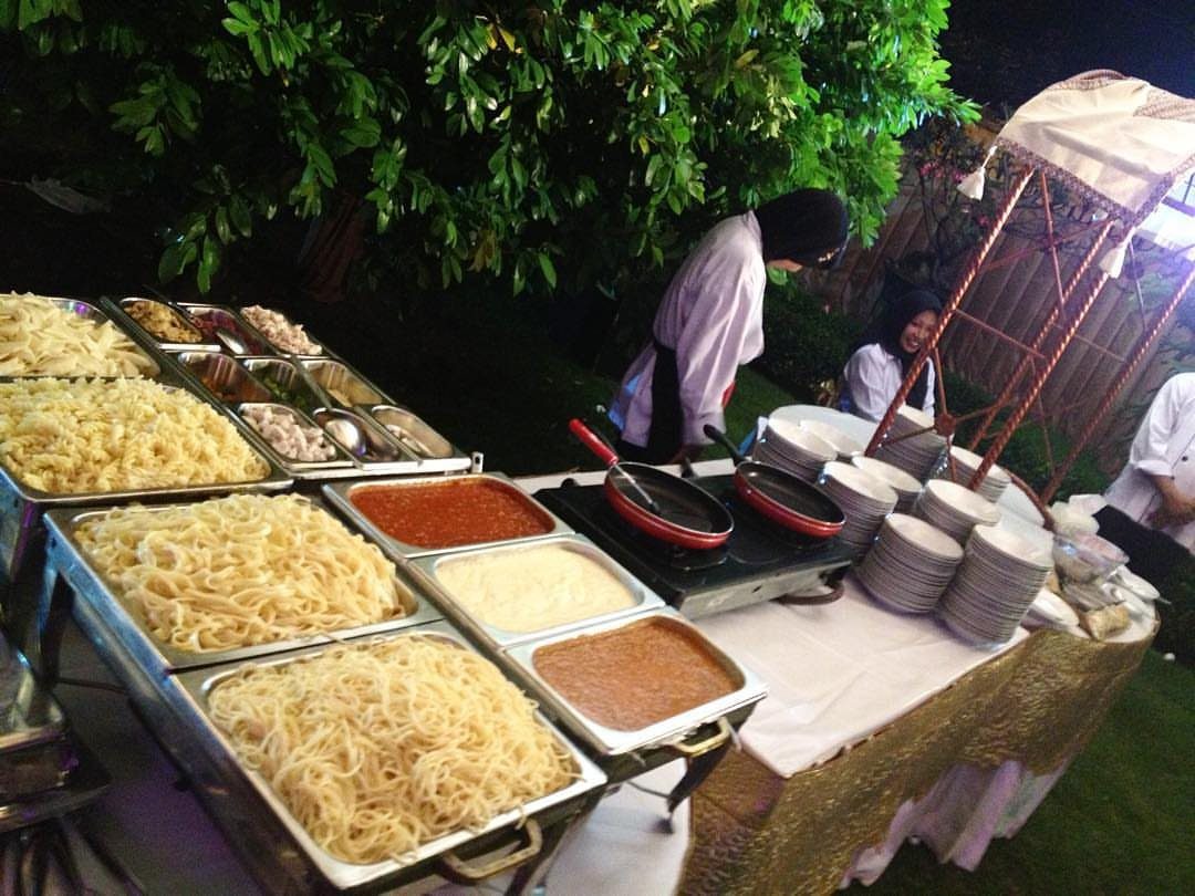 Pasta station with various noodles and sauces in chafing dishes at an event.