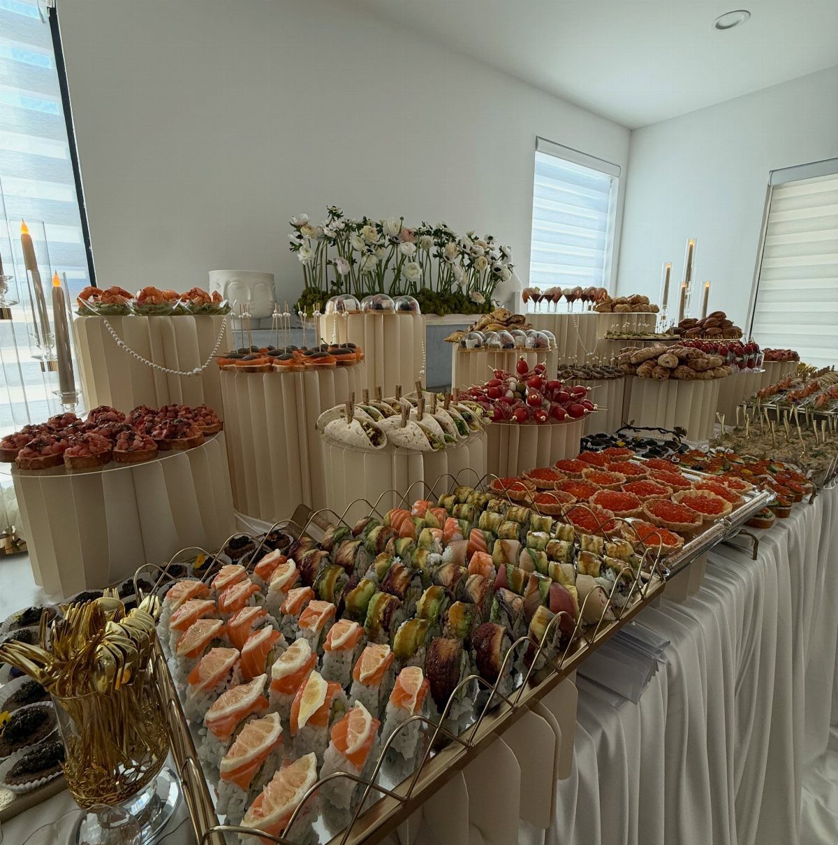 Sushi rolls and assorted appetizers arranged on tiered pedestals at a wedding buffet.