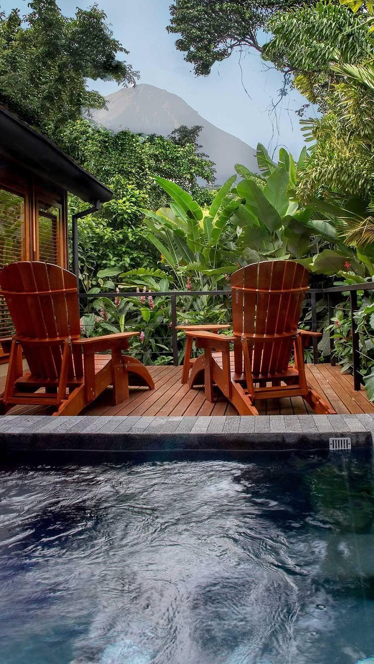 Wooden chairs on a deck with a hot tub overlooking a tropical volcano