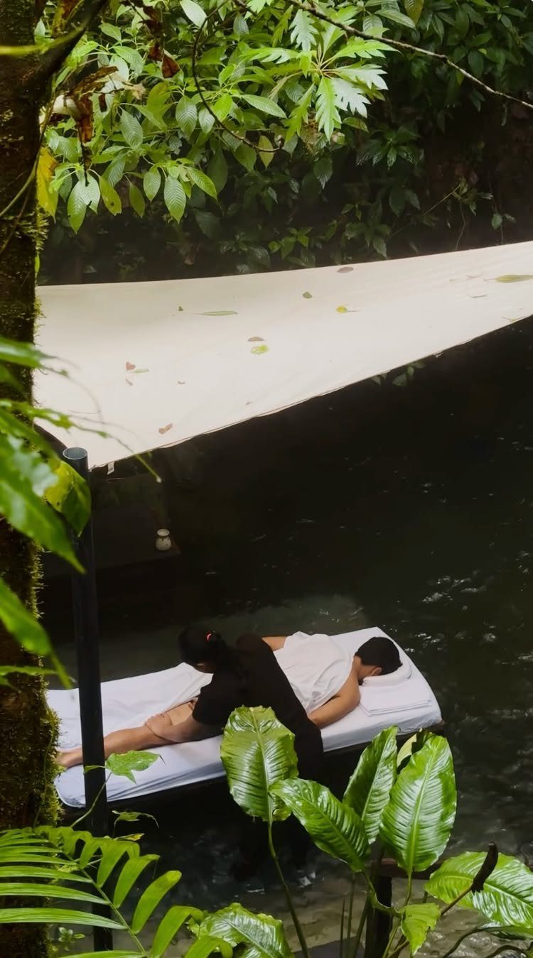 Person receiving a massage on an outdoor platform surrounded by lush tropical jungle foliage