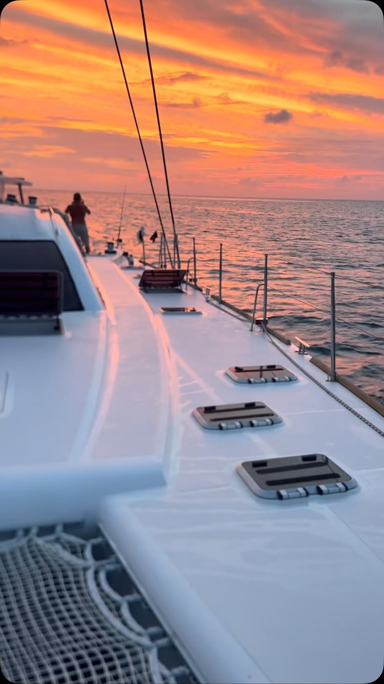 White catamaran deck overlooking a vibrant orange and pink ocean sunset.