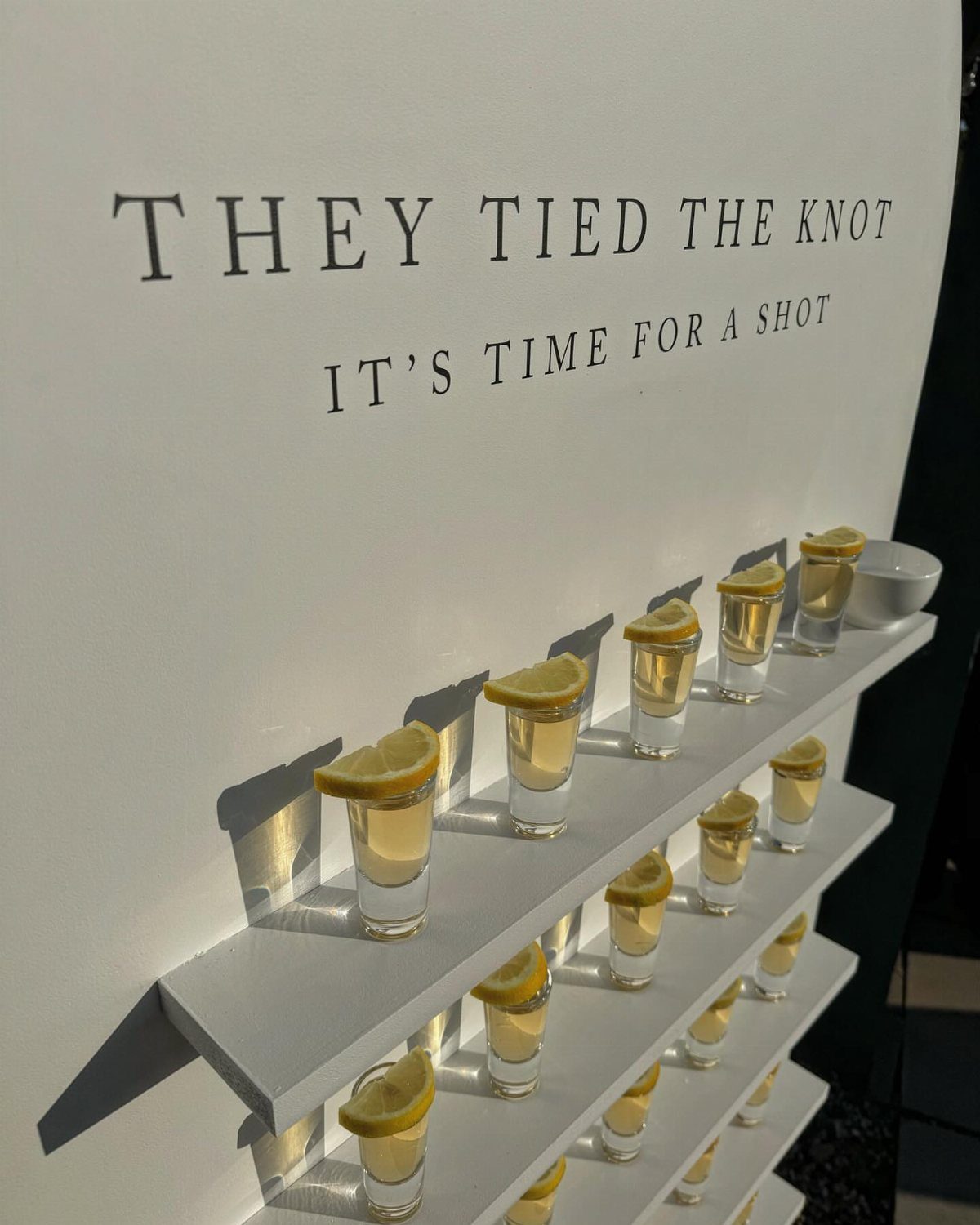 Shot glasses with lemon wedges on white shelves under wedding celebration text