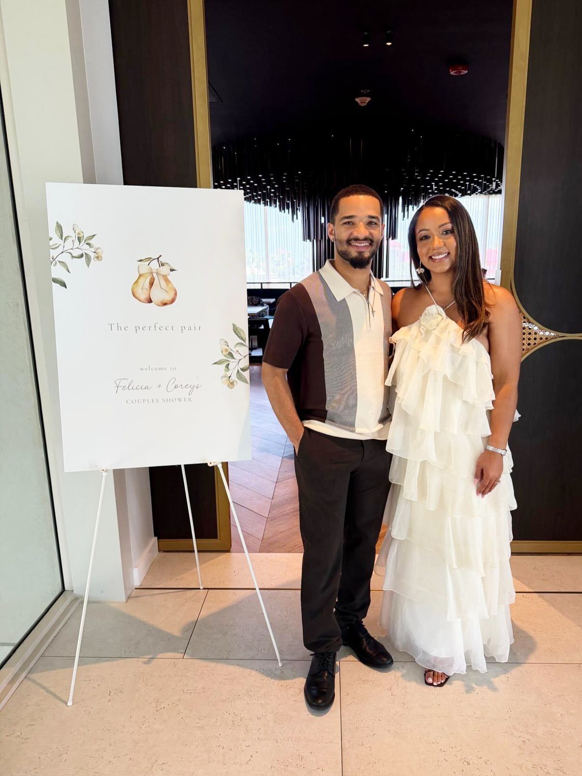 Smiling couple standing next to a white welcome sign in a modern entryway.