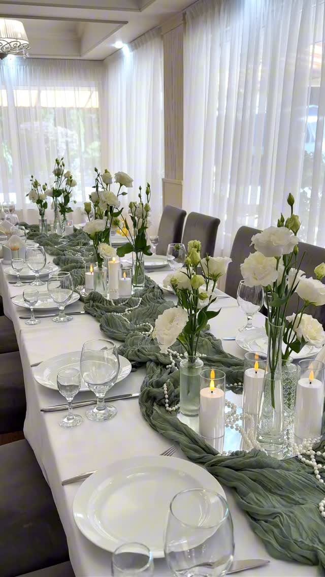 Elegant dinner table setting with white roses, candles, and sage green runner.