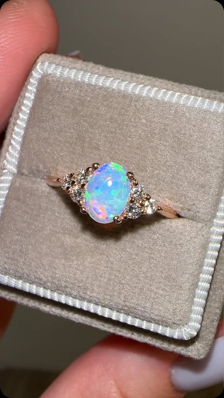 Rose gold ring with a central oval opal and side diamonds in a box