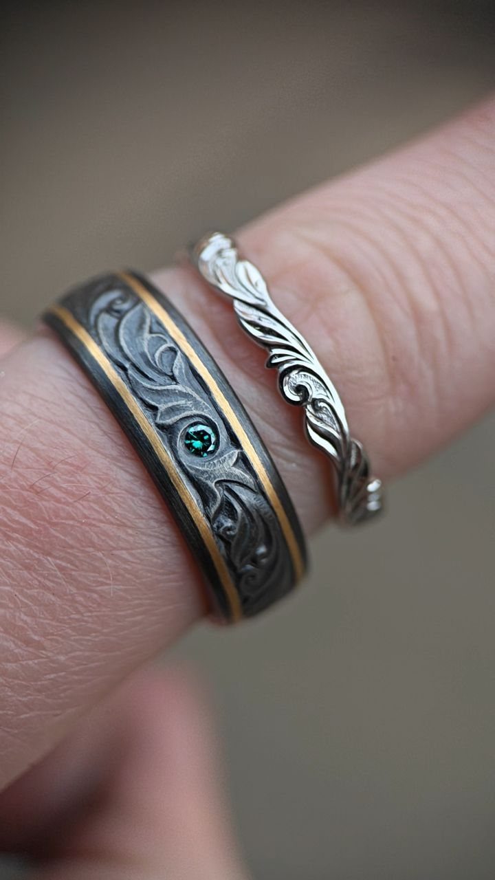 Two ornate wedding rings, one black with gold and one silver, on a finger