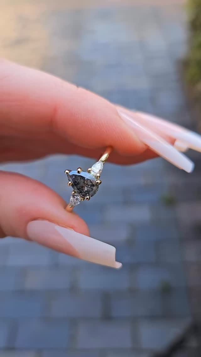 Gold ring with a pear-shaped salt and pepper diamond held by manicured fingers.