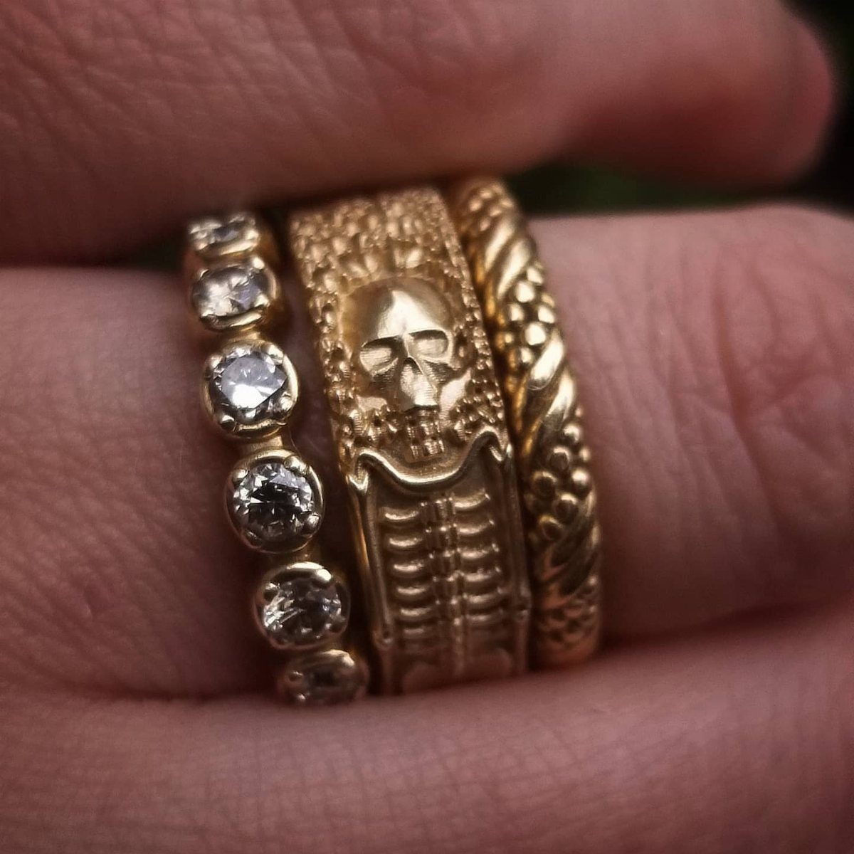 Three gold rings on a finger, including a skull design and braided band.