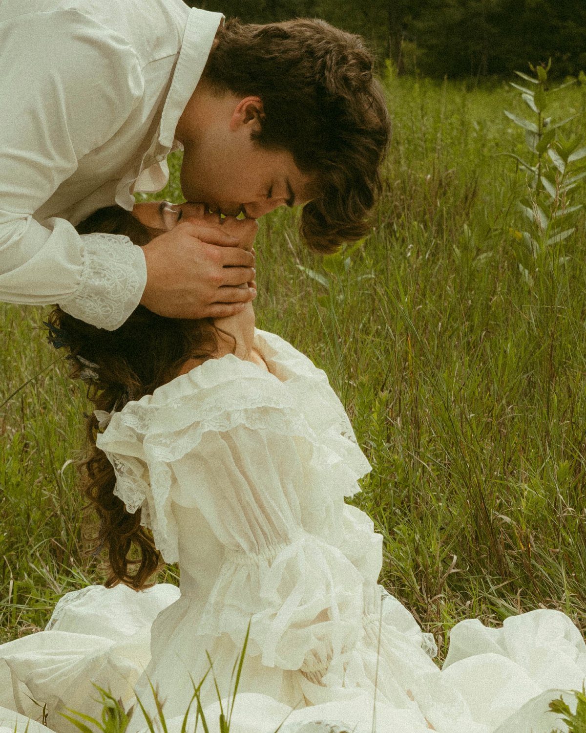 Couple in white clothing sharing an intimate moment in a grassy field