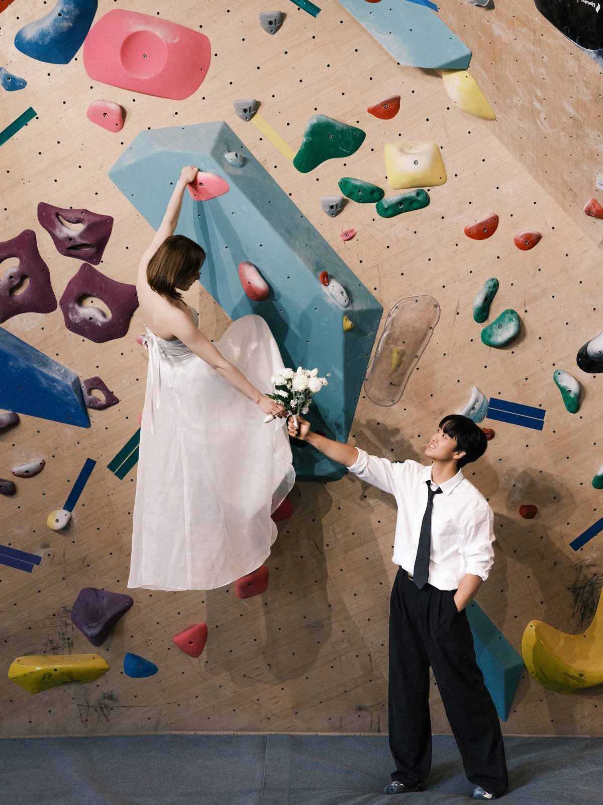 Couple in wedding attire posing on a colorful indoor rock climbing wall.