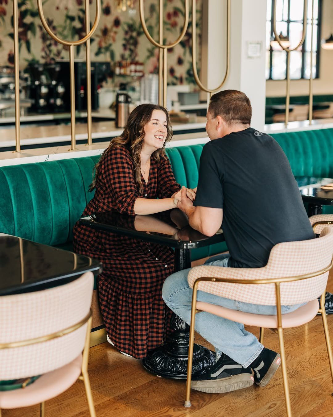 Couple holding hands and smiling at each other inside a cozy cafe setting.