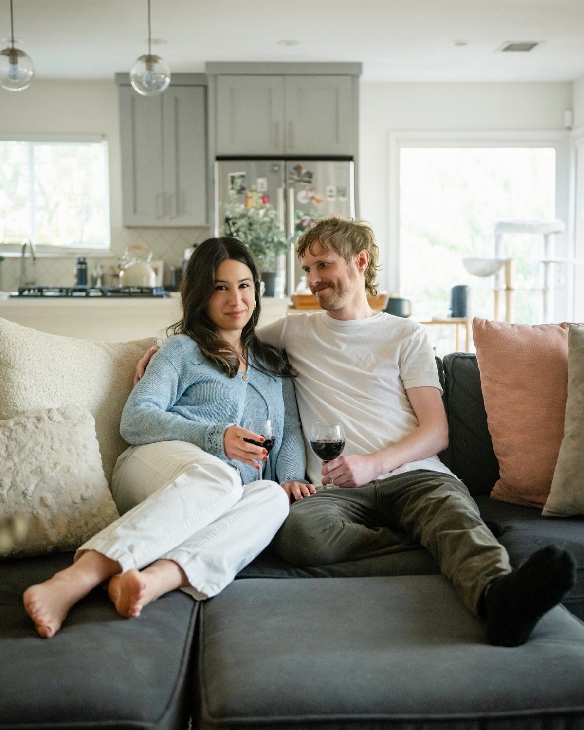 Couple sitting on a grey sofa holding red wine in a modern home.