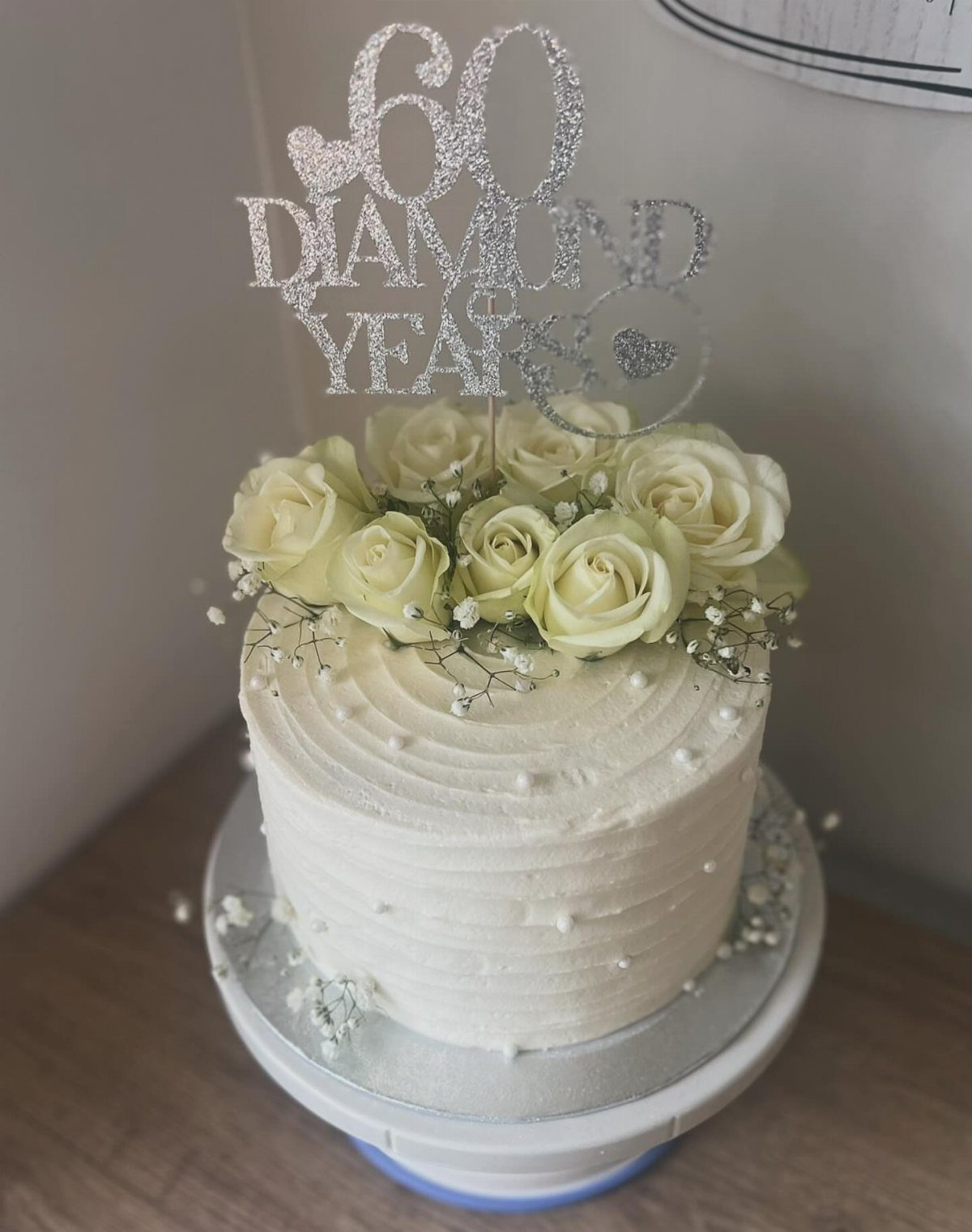 White frosted cake with cream roses and a silver 60 diamond years topper.