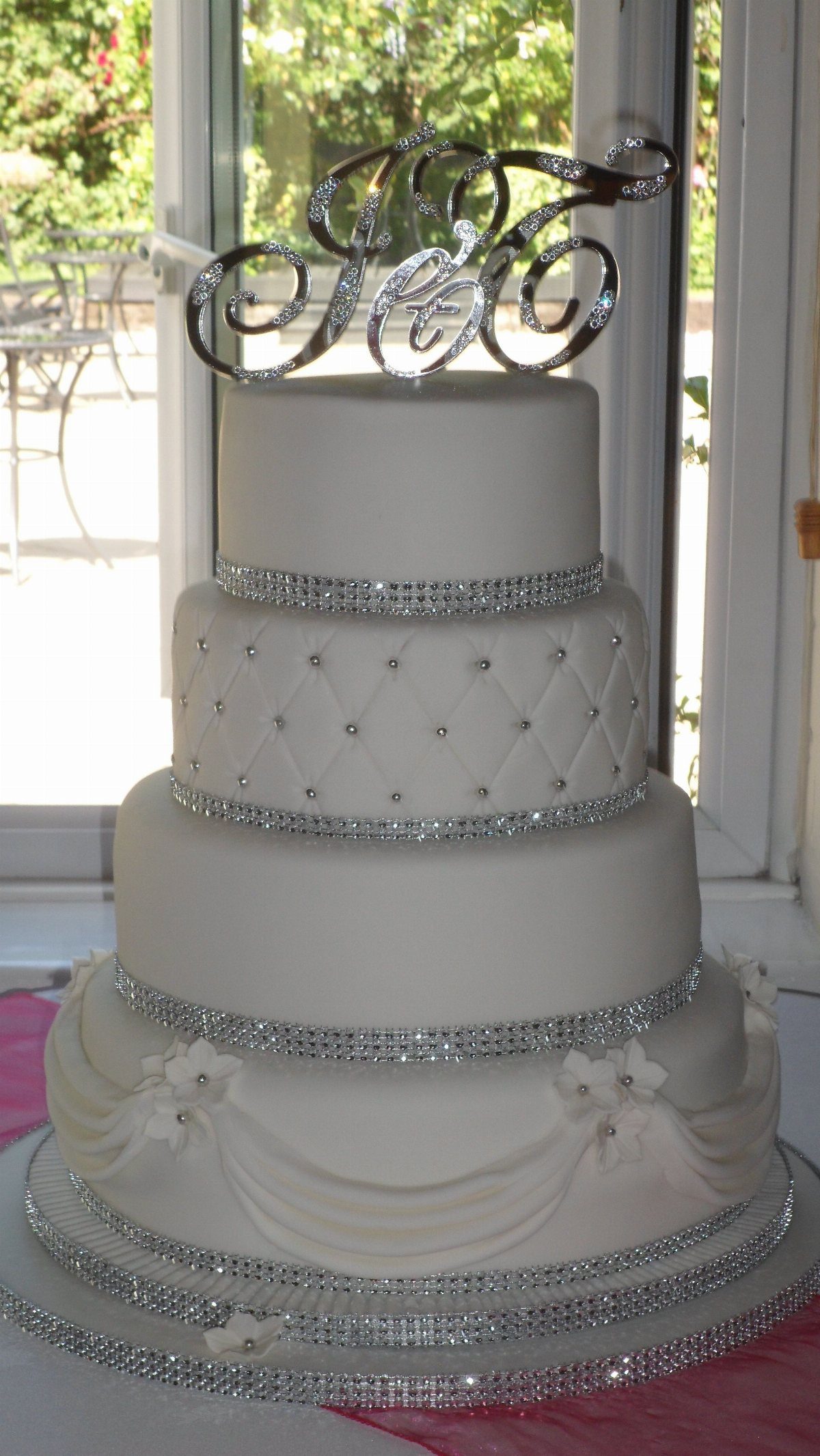 Four-tier white wedding cake with rhinestone bands, quilted patterns, and draped fondant swags.