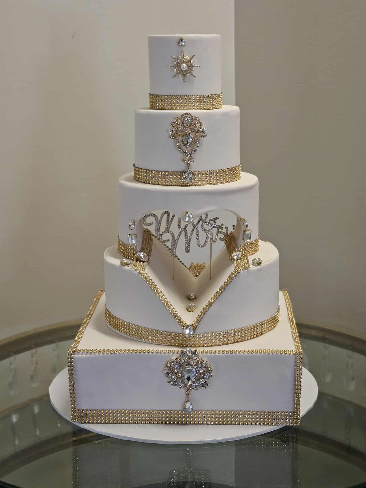 Five-tier white cake decorated with gold rhinestone bands and crystal jewelry ornaments.