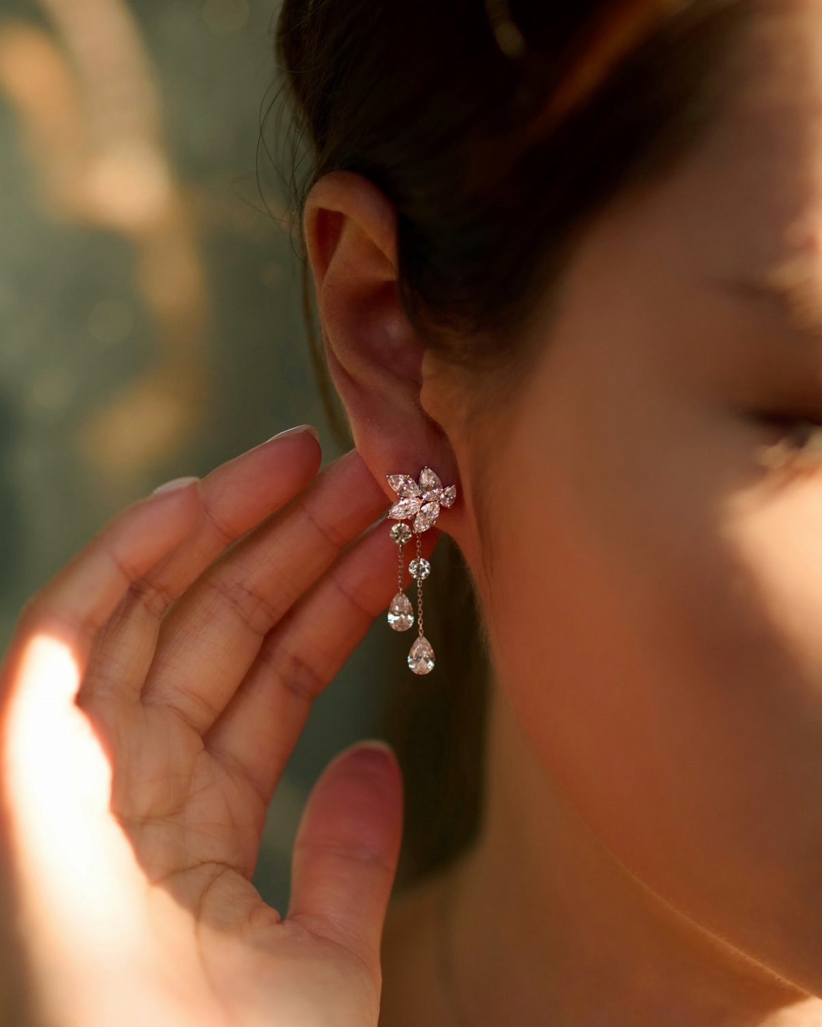 Dangling diamond earrings with floral studs worn by a woman in sunlight