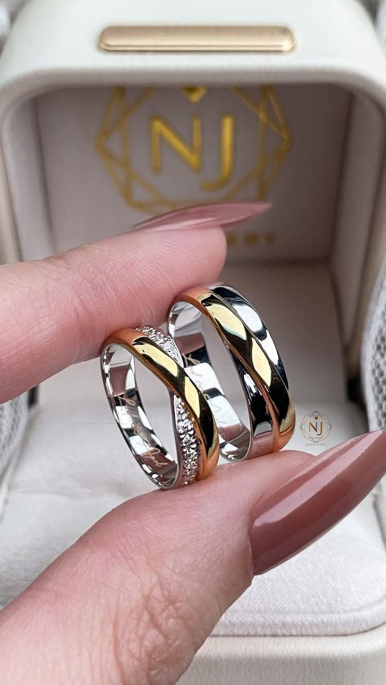 Two two-tone gold and silver wedding bands with diamonds held by manicured fingers.