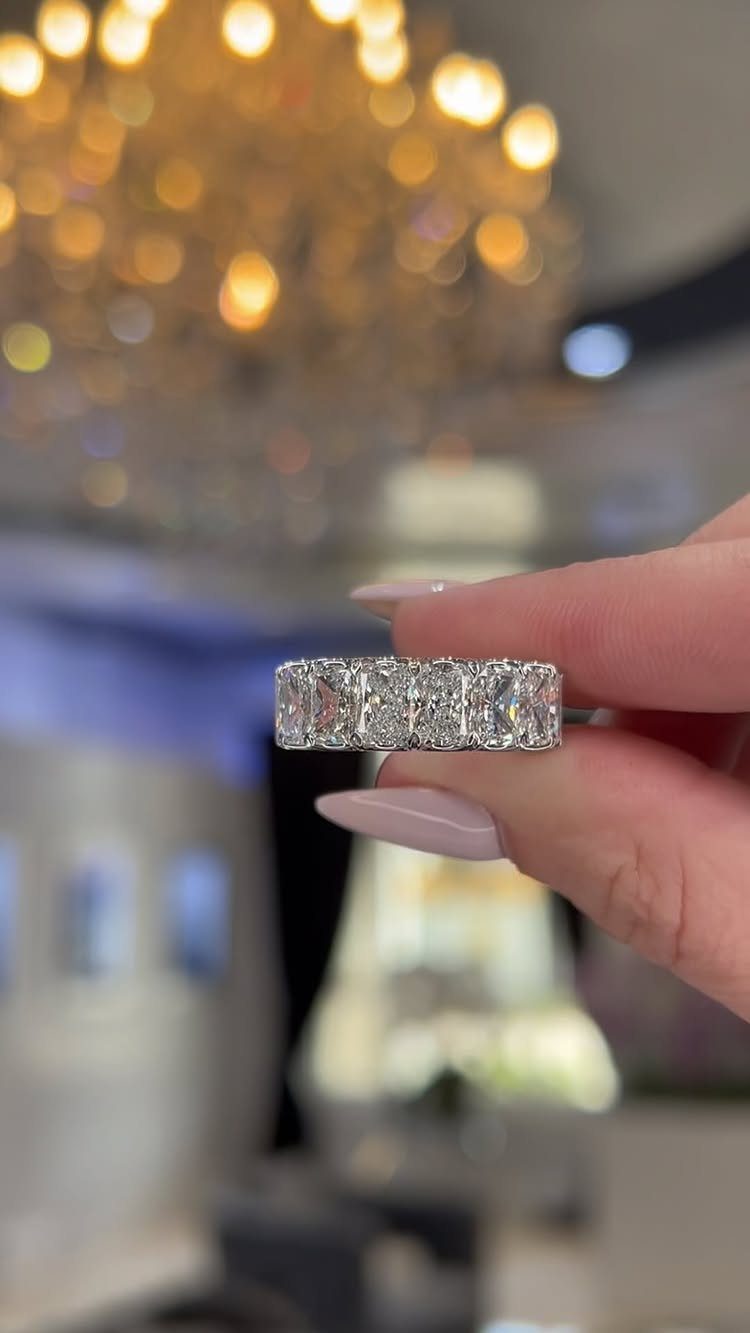 Diamond eternity band with square-cut stones held by a hand with manicured nails.